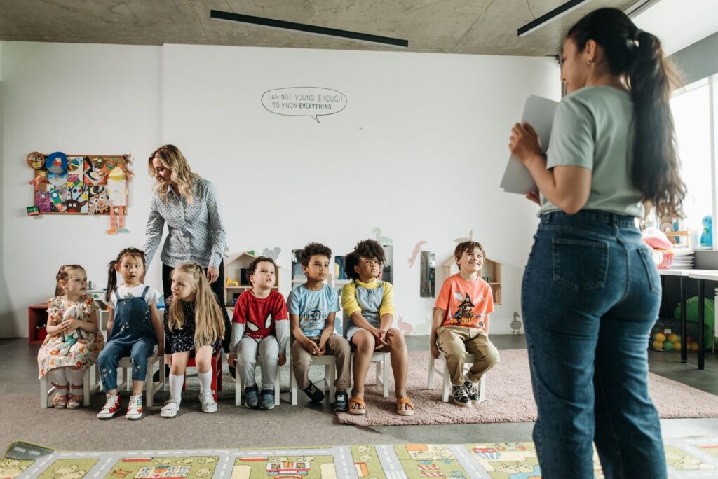 Two preschool teachers leading a group of children in a bright classroom