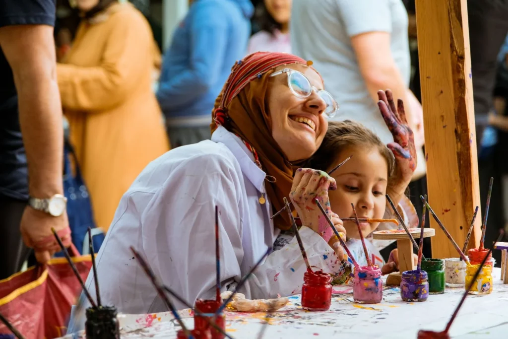 Smiling woman and young girl painting together at an outdoor community art table